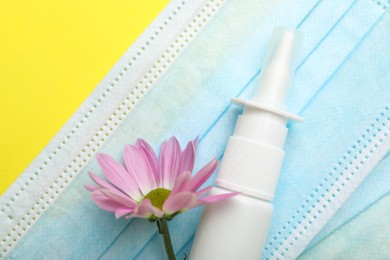 Photo of Allergy treatment. Nasal spray, protective masks and flower on yellow background, top view