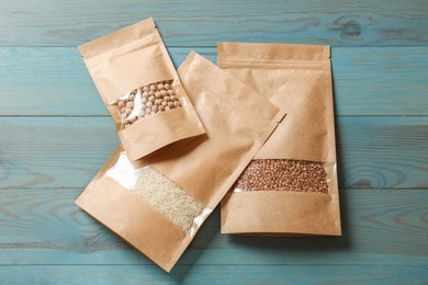 Photo of Paper pouch bags with buckwheat, chickpeas and rice on light blue wooden table, flat lay