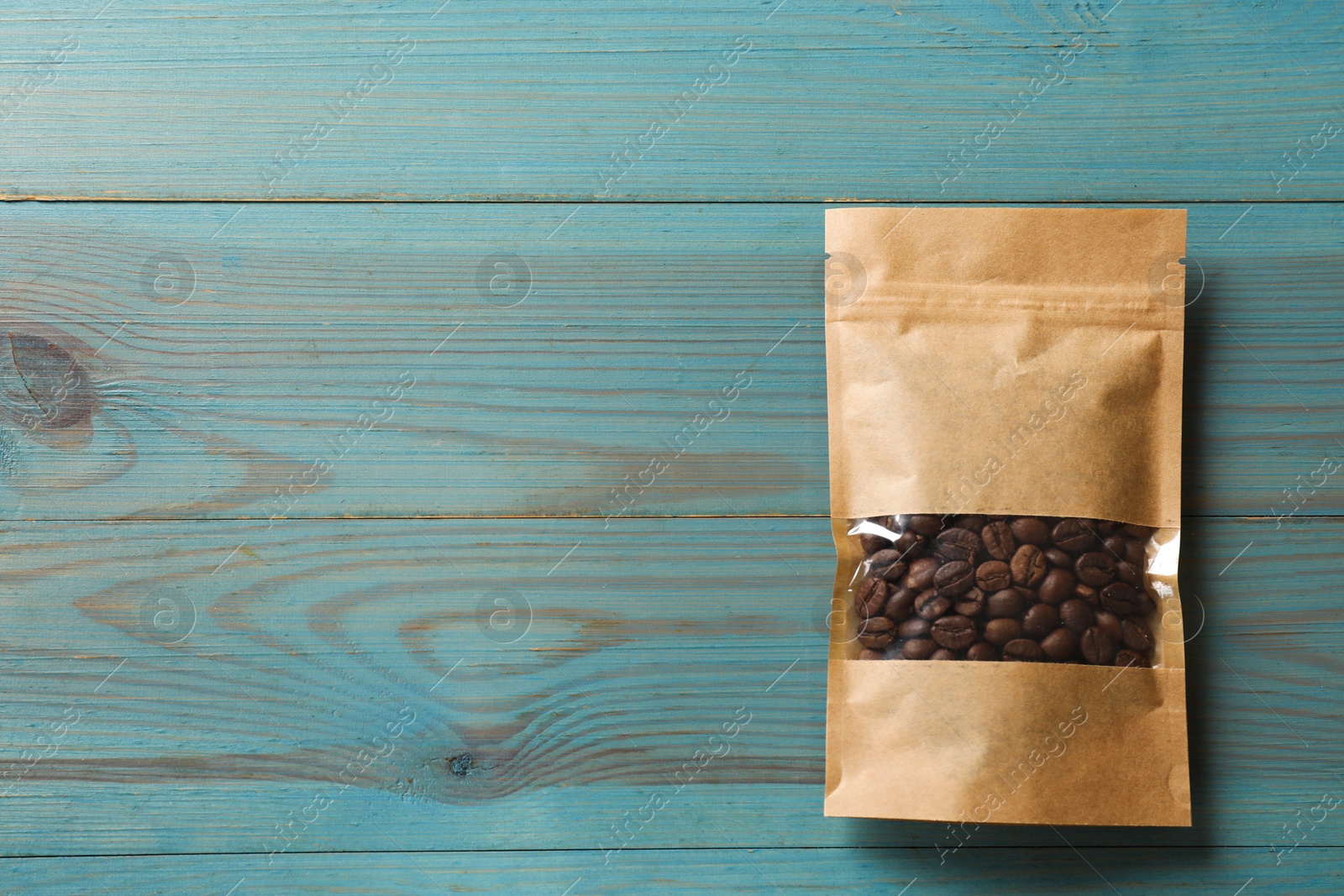 Photo of Paper pouch bag with coffee beans on light blue wooden table, top view. Space for text