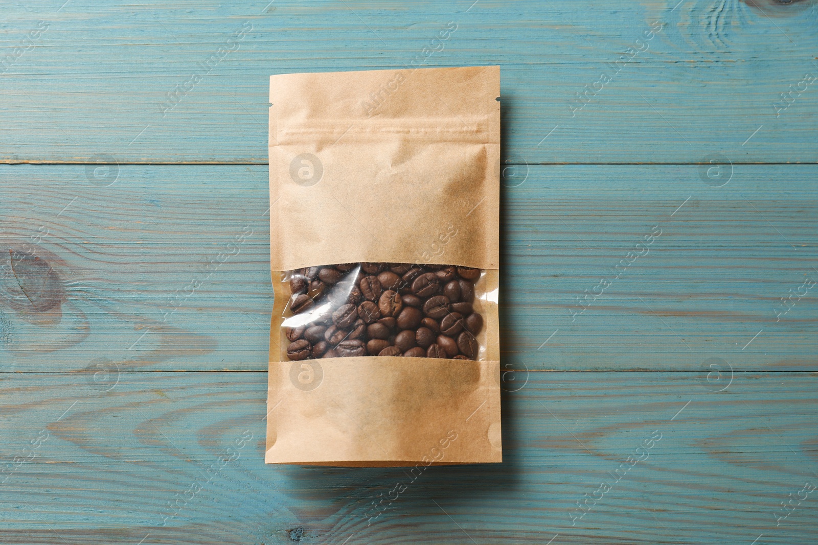 Photo of Paper pouch bag with coffee beans on light blue wooden table, top view