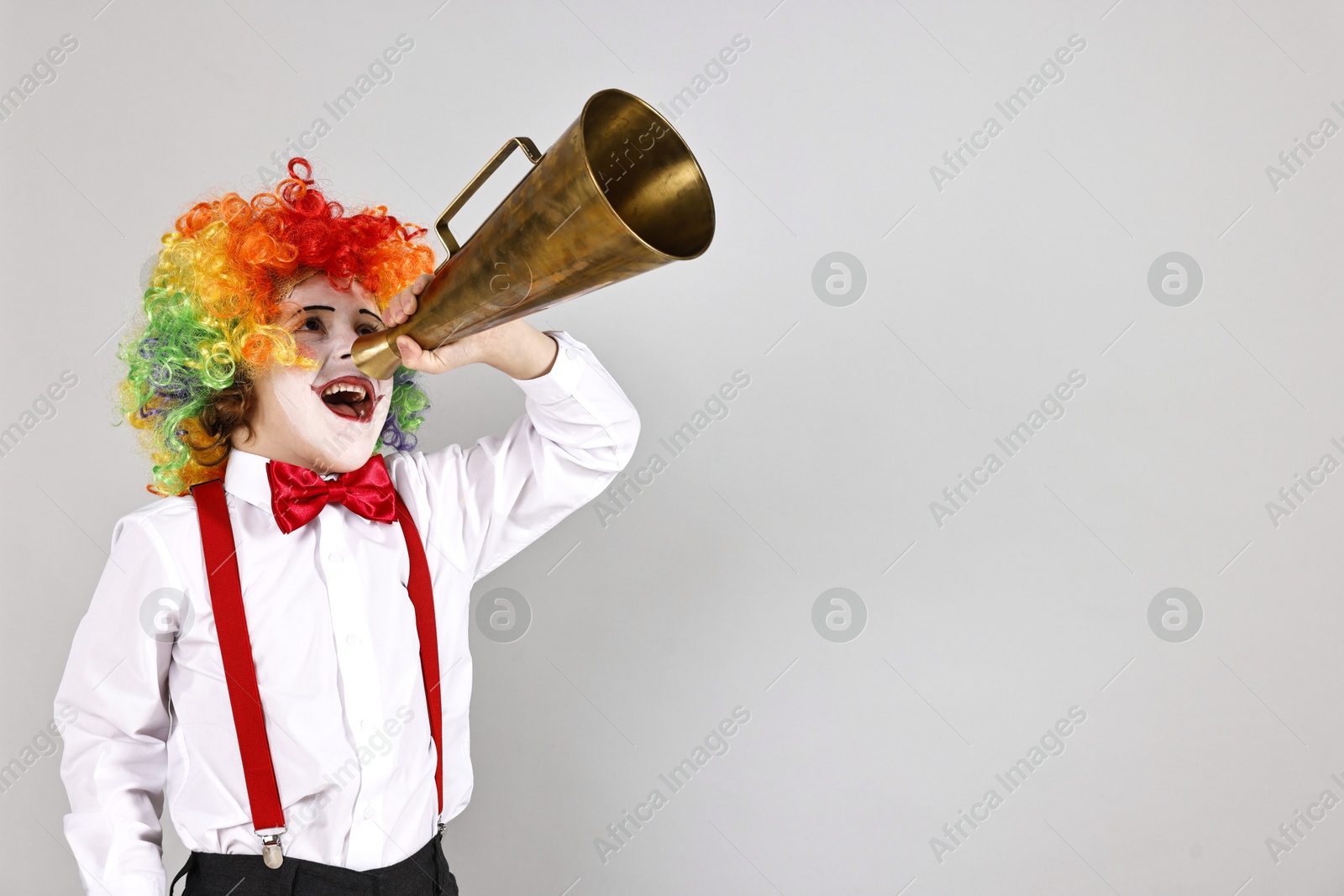 Photo of Little boy dressed like clown shouting in megaphone on grey background, space for text. Surprise party