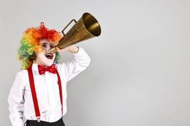 Photo of Little boy dressed like clown shouting in megaphone on grey background, space for text. Surprise party