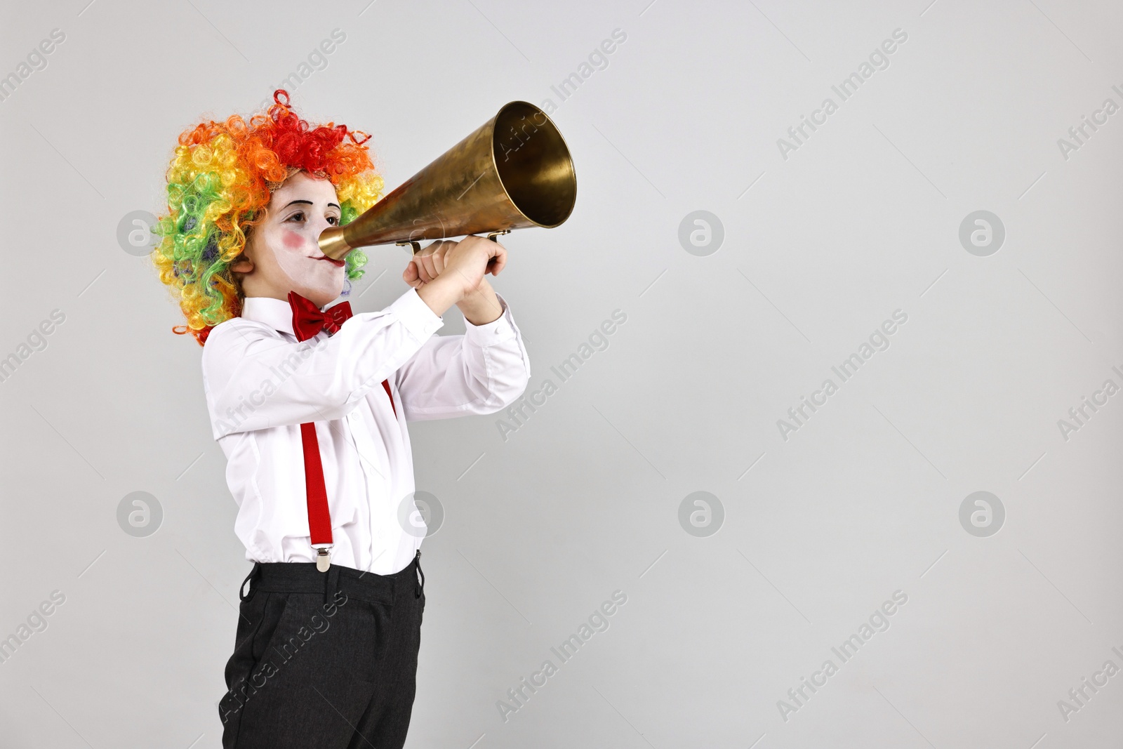 Photo of Little boy dressed like clown with megaphone on grey background, space for text. Surprise party