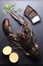 Photo of Raw lobster, cut lemon, microgreens and spices on dark textured table, flat lay