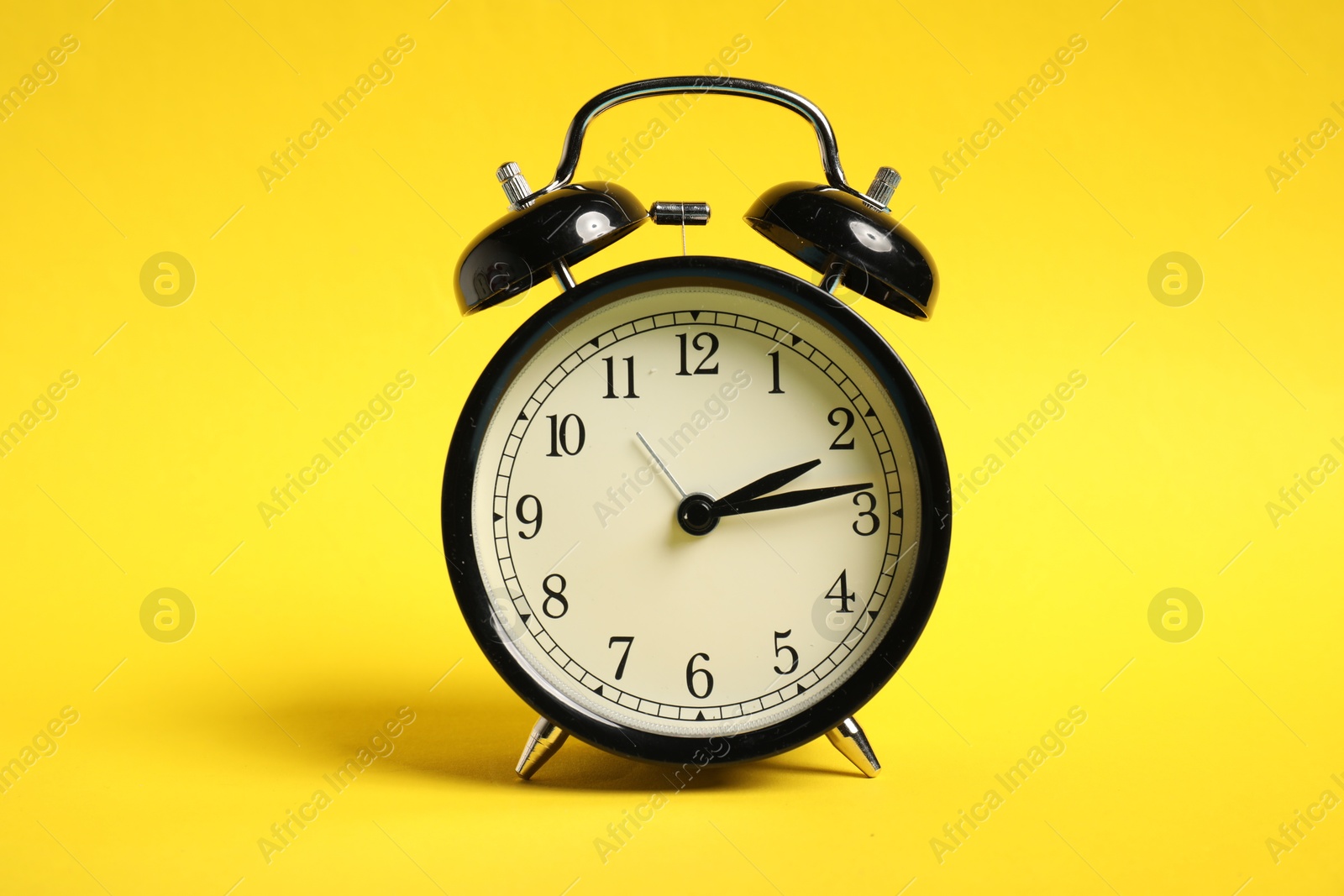 Photo of One black alarm clock on yellow background