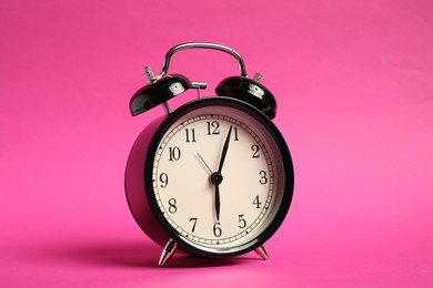 Photo of One black alarm clock on bright pink background