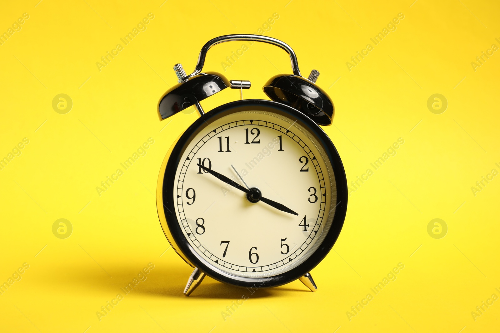 Photo of One black alarm clock on yellow background