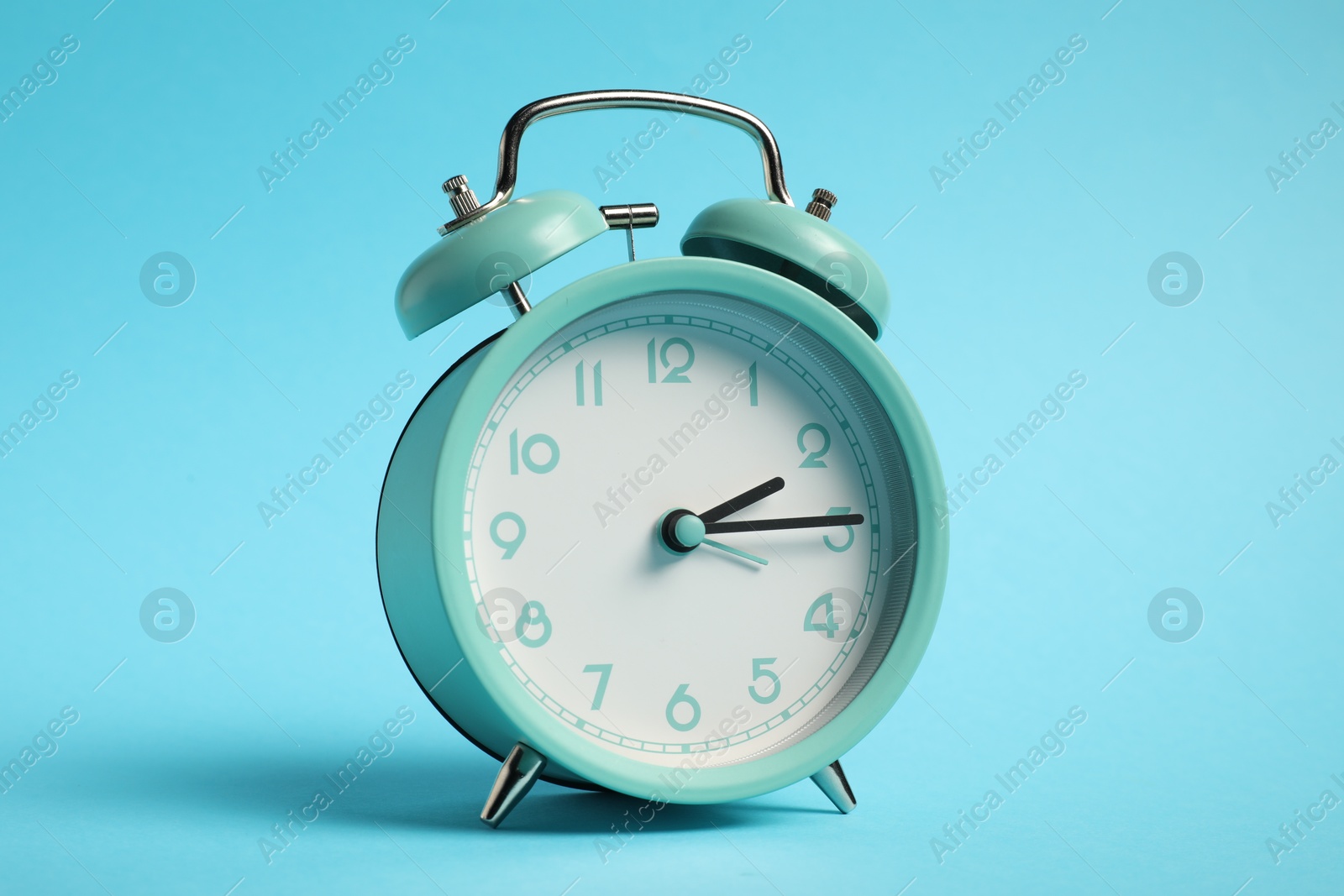 Photo of One turquoise alarm clock on light blue background