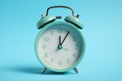 Photo of One turquoise alarm clock on light blue background