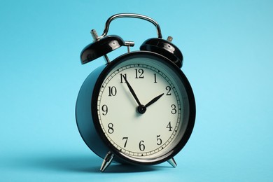 Photo of One black alarm clock on light blue background