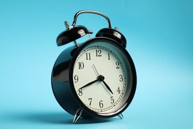 Photo of One black alarm clock on light blue background