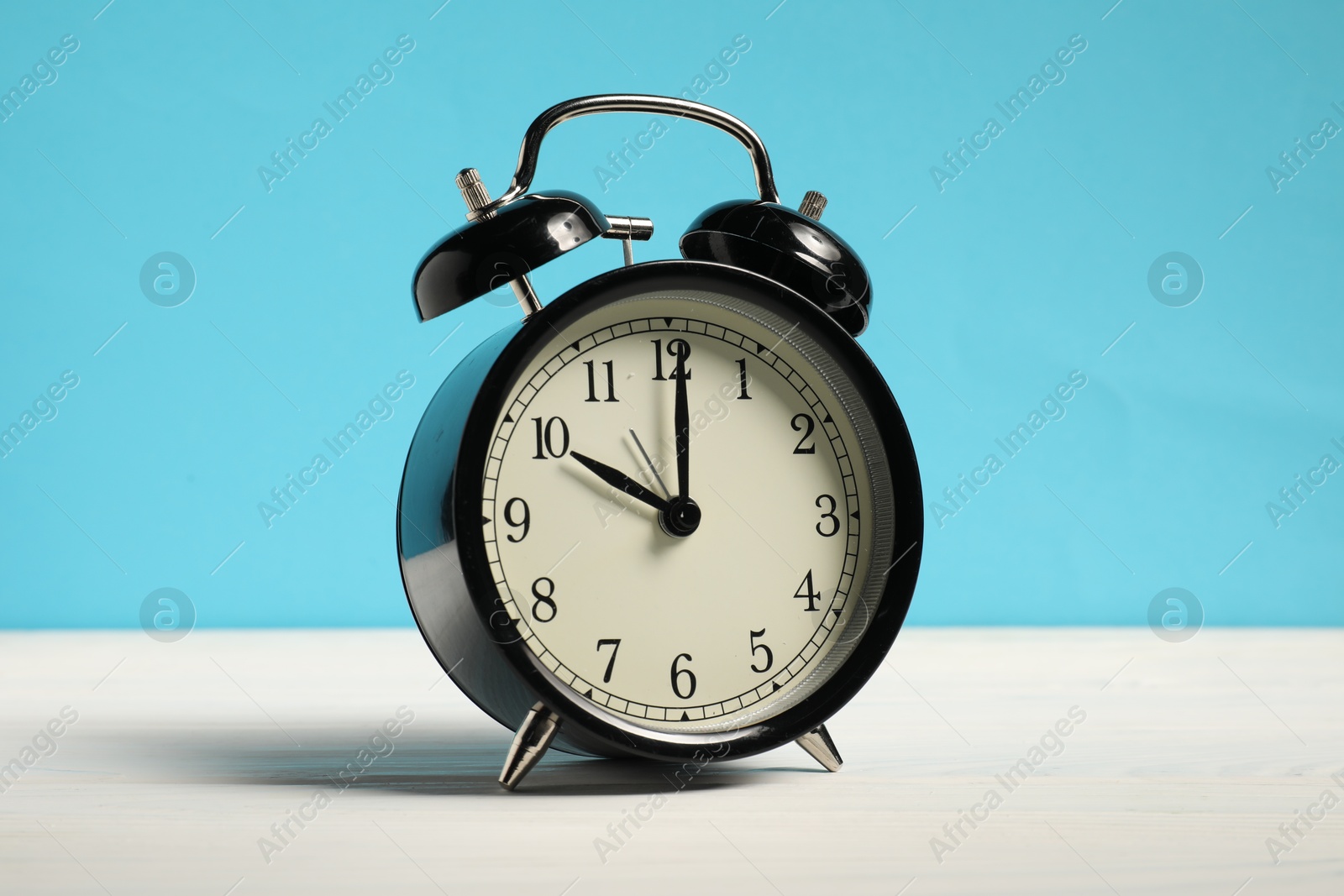 Photo of One black clock on white wooden table against light blue background