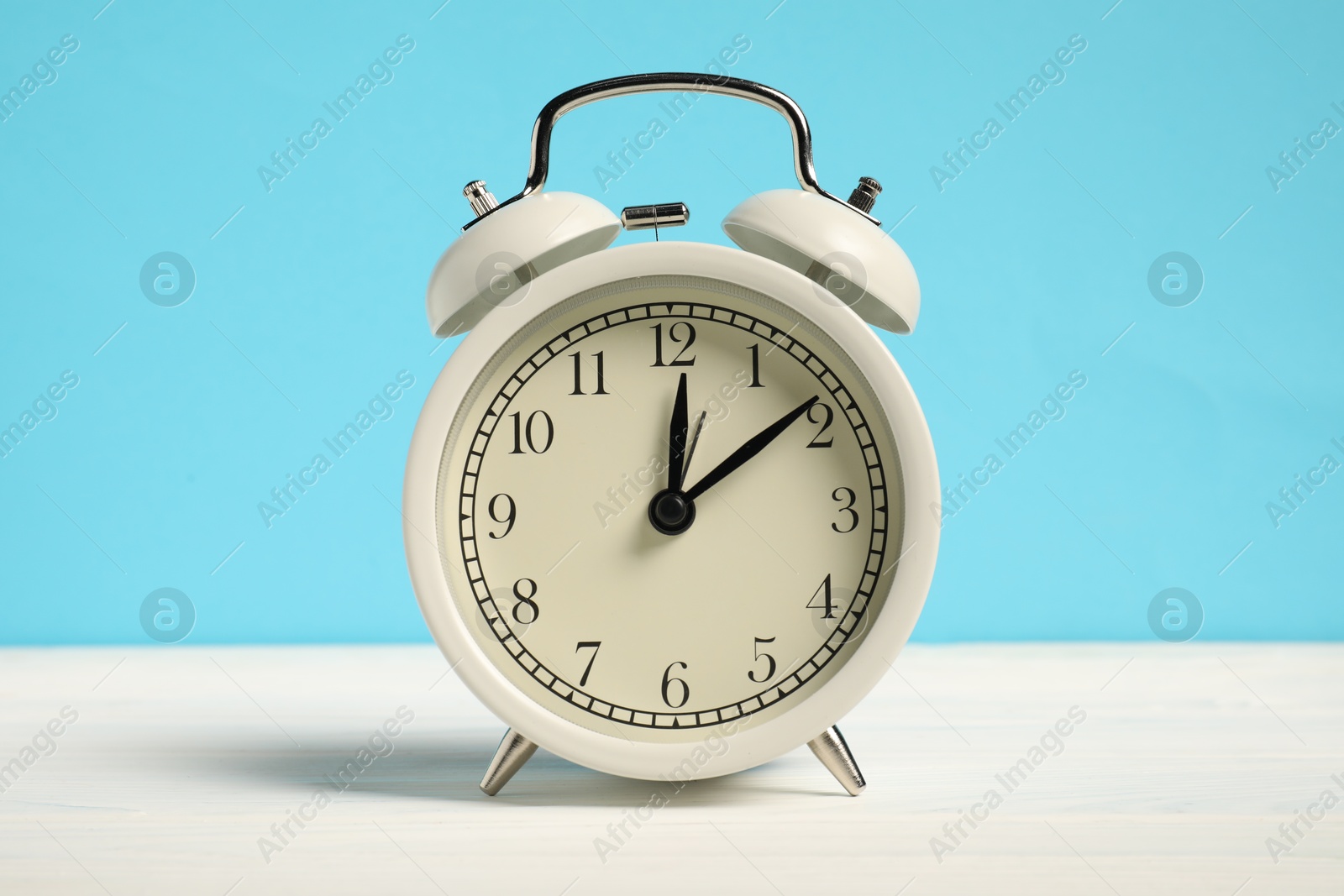 Photo of One alarm clock on white wooden table against light blue background