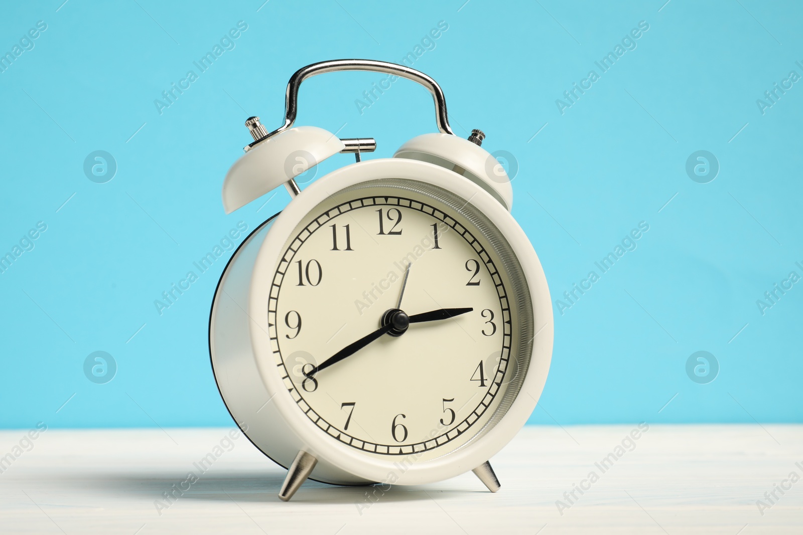 Photo of One alarm clock on white wooden table against light blue background