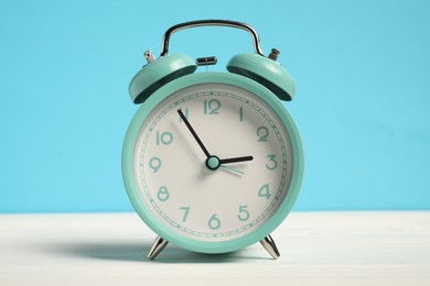 Photo of One turquoise alarm clock on white wooden table against light blue background