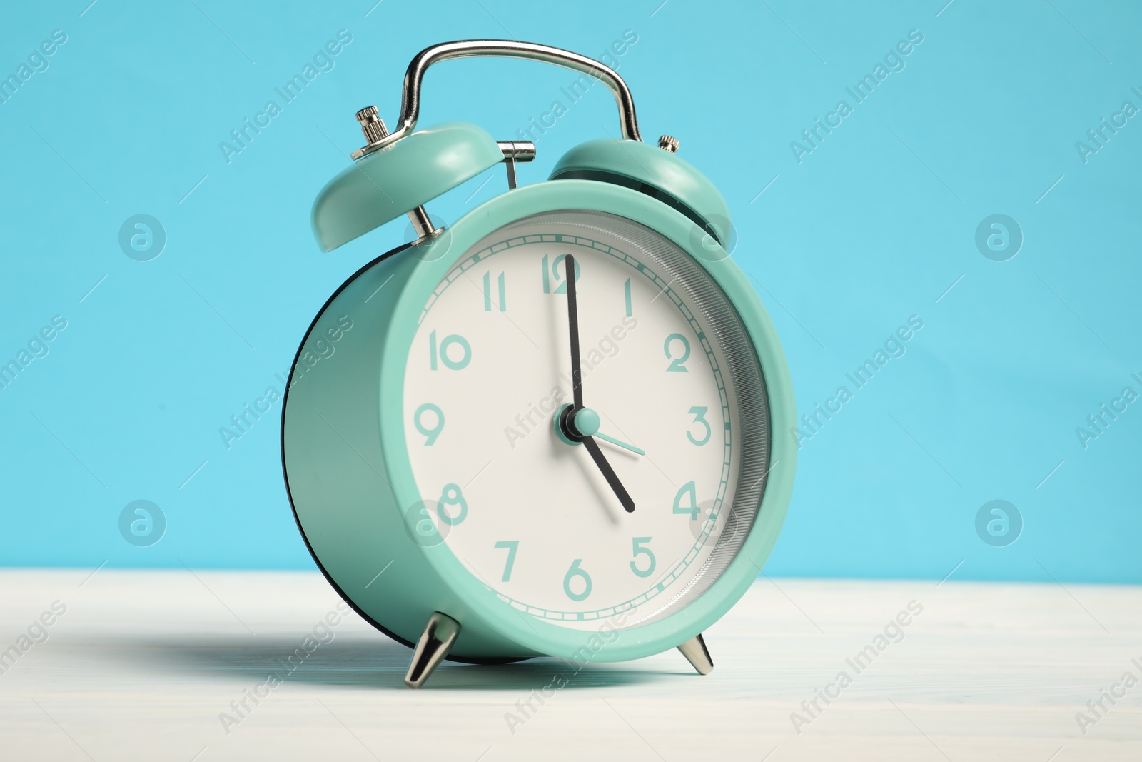 Photo of One turquoise alarm clock on white wooden table against light blue background