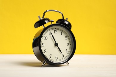 Photo of One black alarm clock on white wooden table against yellow background