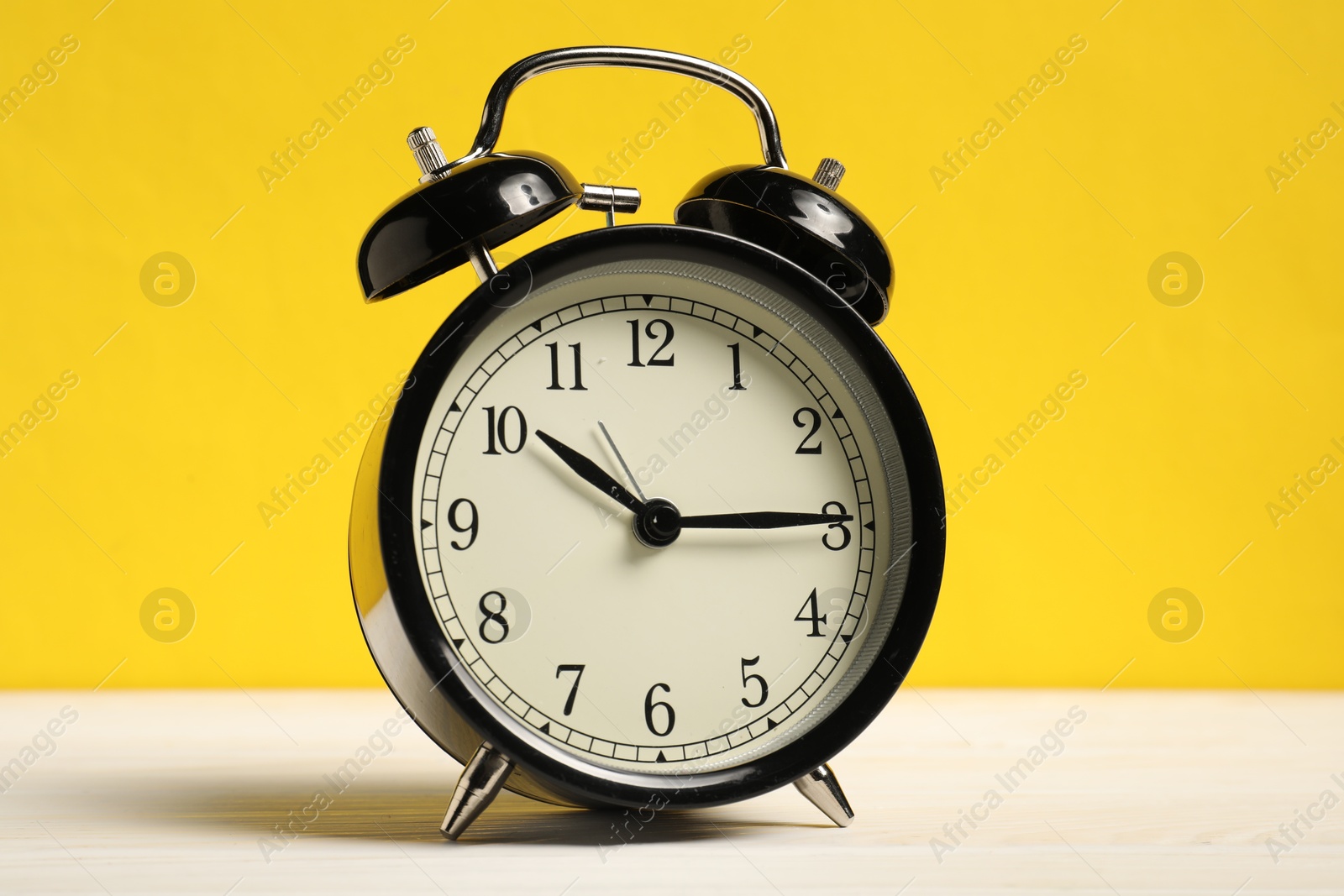 Photo of One black alarm clock on white wooden table against yellow background