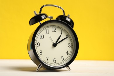 Photo of One black alarm clock on white wooden table against yellow background