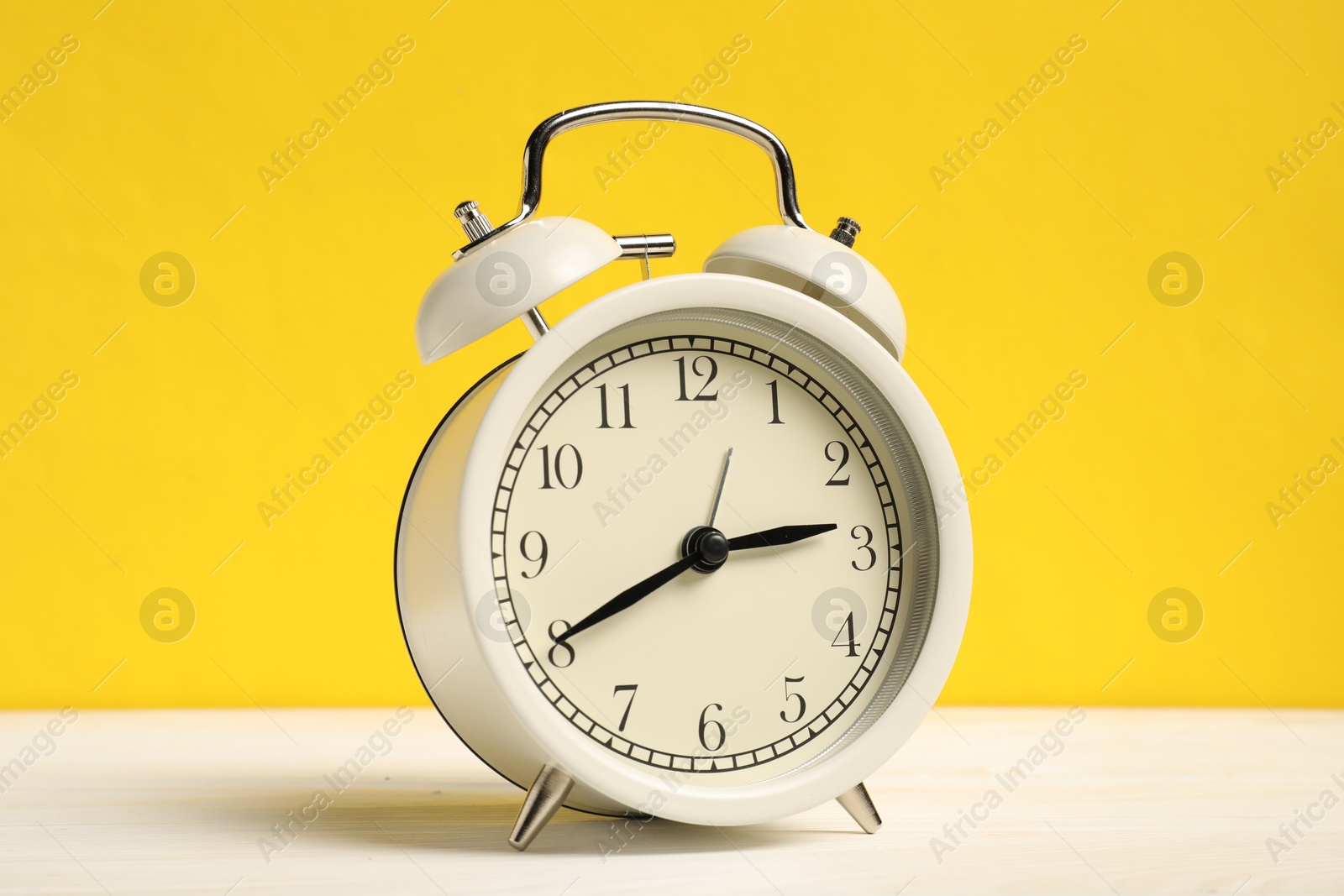 Photo of One alarm clock on white wooden table against yellow background