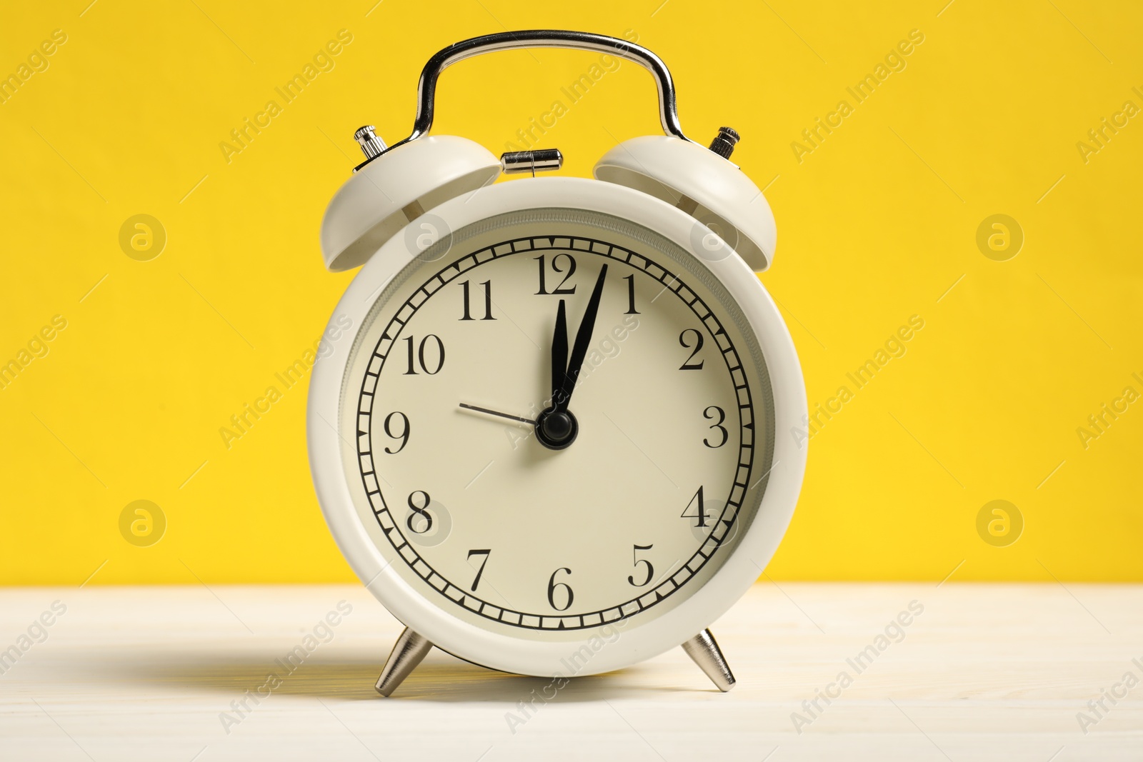 Photo of One alarm clock on white wooden table against yellow background