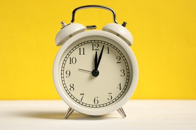 Photo of One alarm clock on white wooden table against yellow background