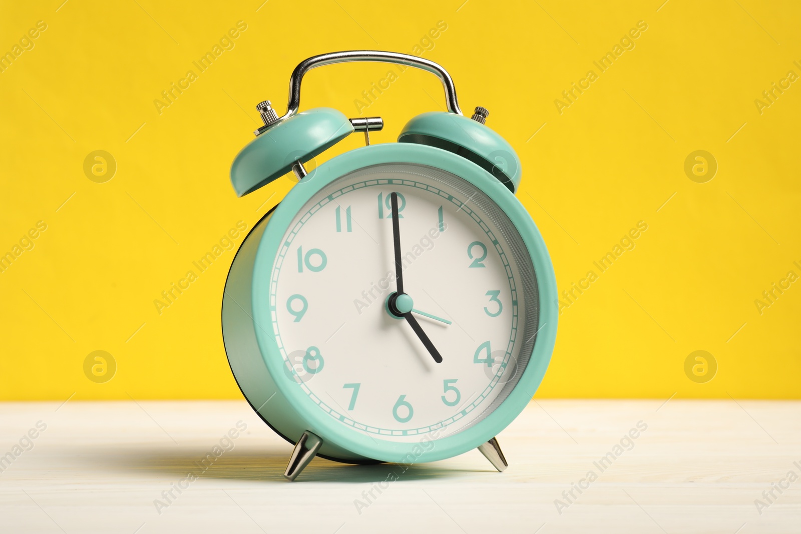 Photo of One turquoise alarm clock on white wooden table against yellow background