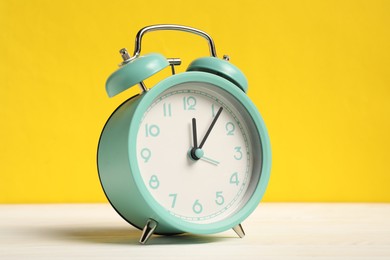 Photo of One turquoise alarm clock on white wooden table against yellow background