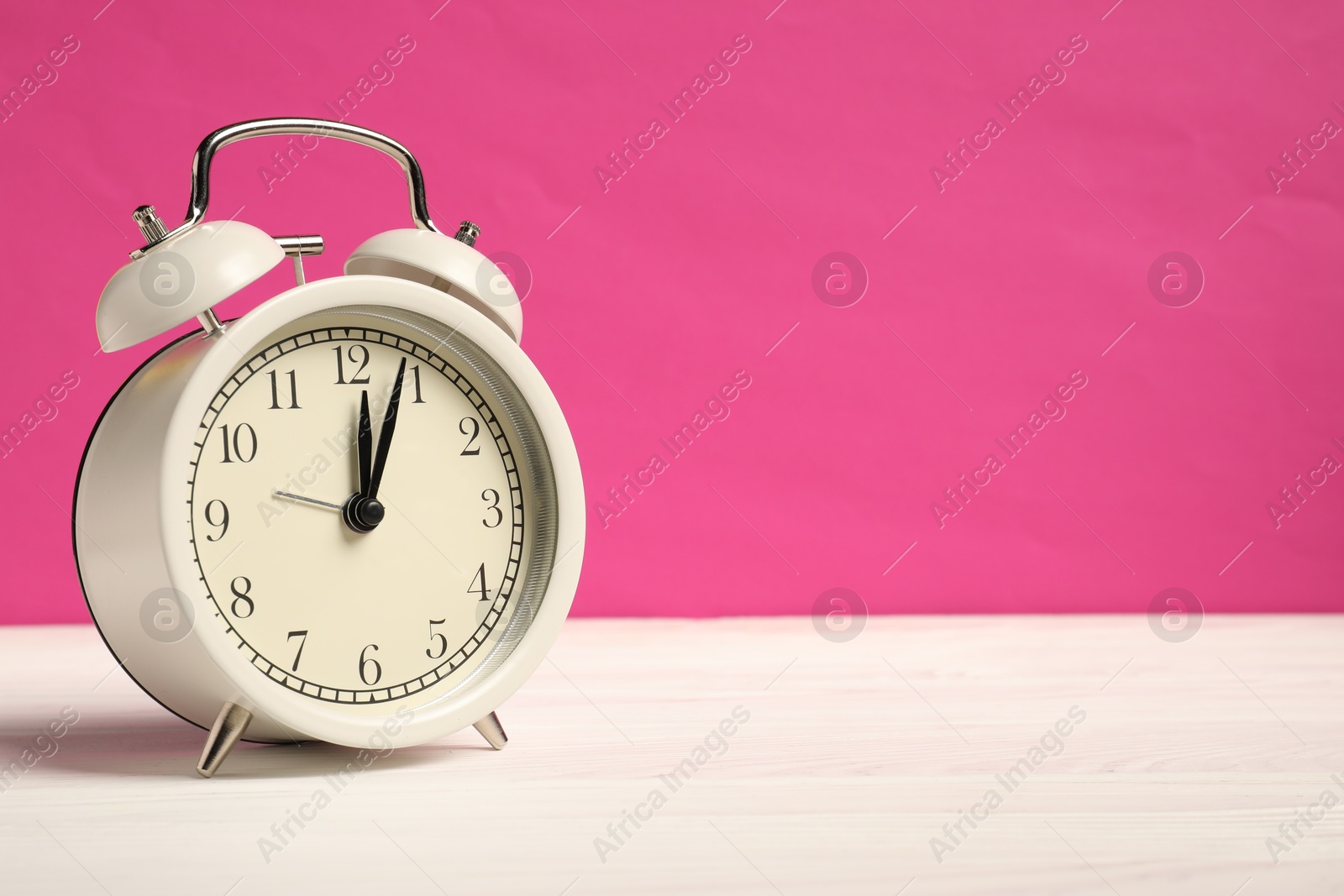 Photo of One alarm clock on white wooden table against bright pink background, space for text