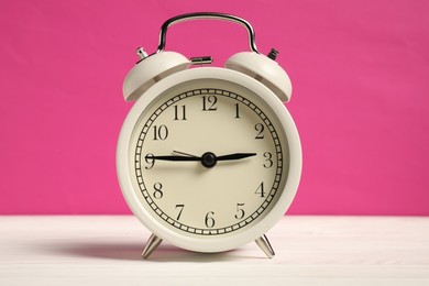 Photo of One alarm clock on white wooden table against bright pink background