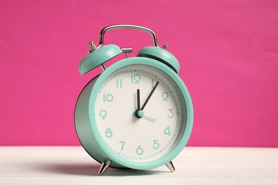 Photo of One turquoise alarm clock on white wooden table against bright pink background