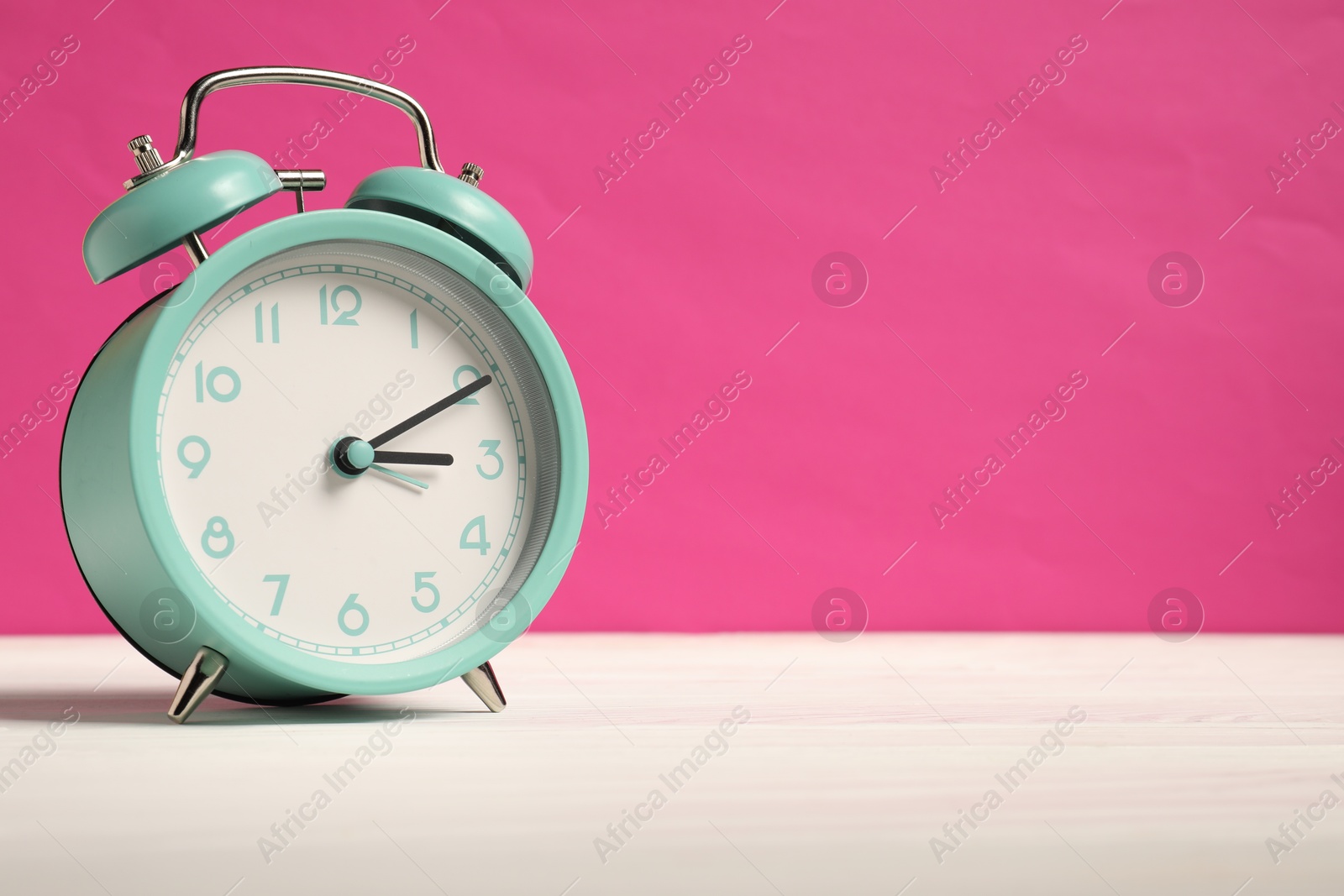 Photo of One turquoise alarm clock on white wooden table against bright pink background, space for text