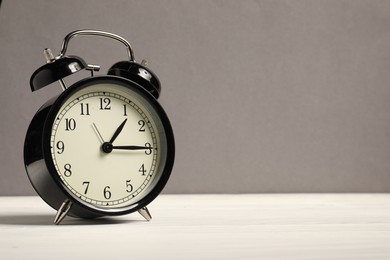 Photo of One black alarm clock on white wooden table against grey background, space for text