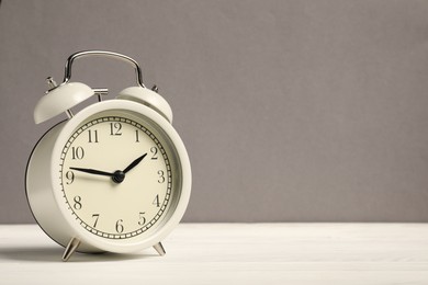 Photo of One alarm clock on white wooden table against grey background, space for text