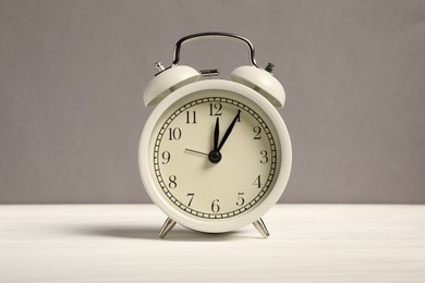 Photo of One alarm clock on white wooden table against grey background