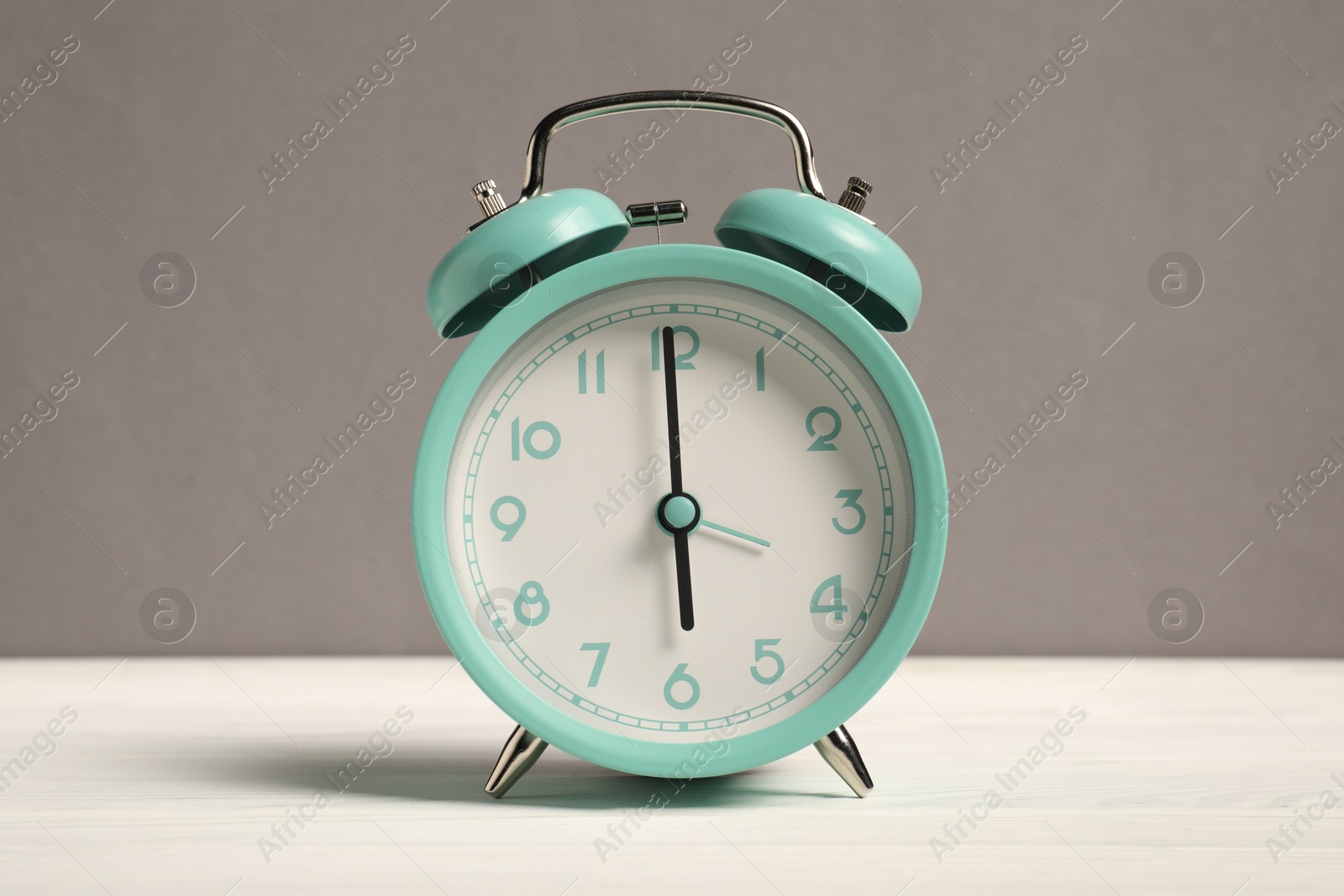 Photo of One turquoise alarm clock on white wooden table against grey background