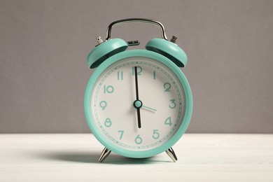 Photo of One turquoise alarm clock on white wooden table against grey background