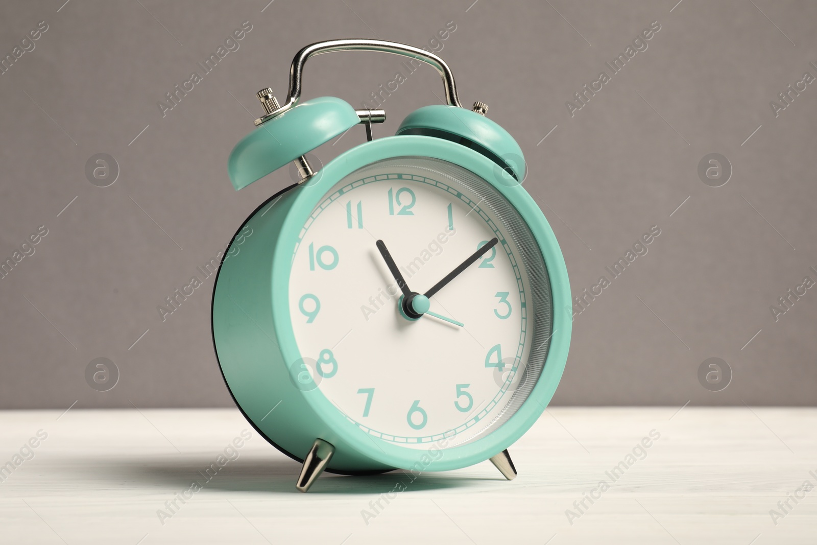 Photo of One turquoise alarm clock on white wooden table against grey background