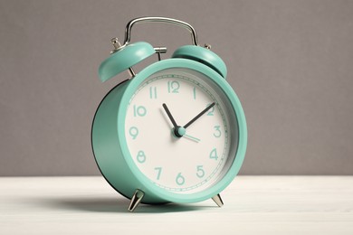 Photo of One turquoise alarm clock on white wooden table against grey background