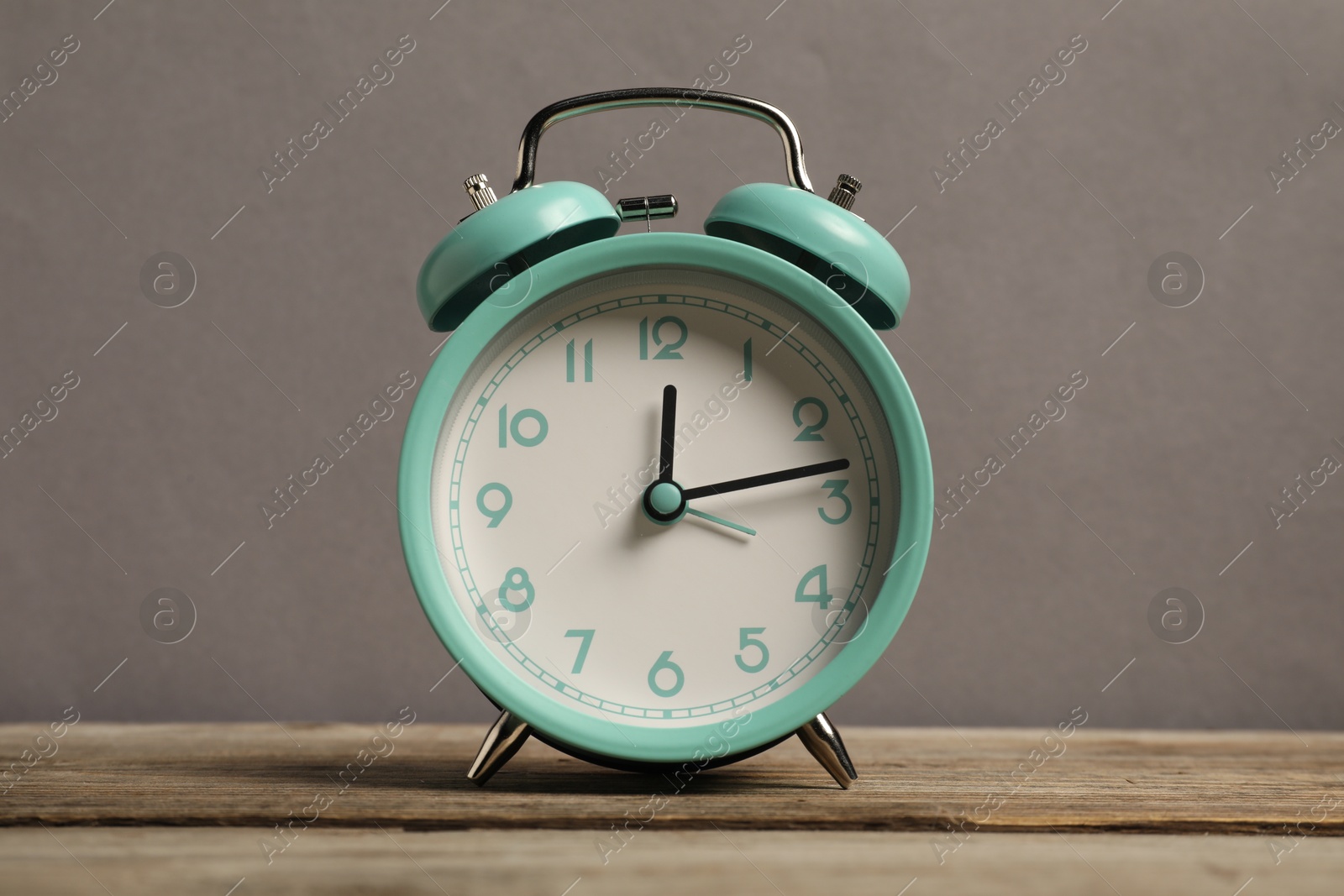 Photo of One turquoise alarm clock on wooden table against grey background