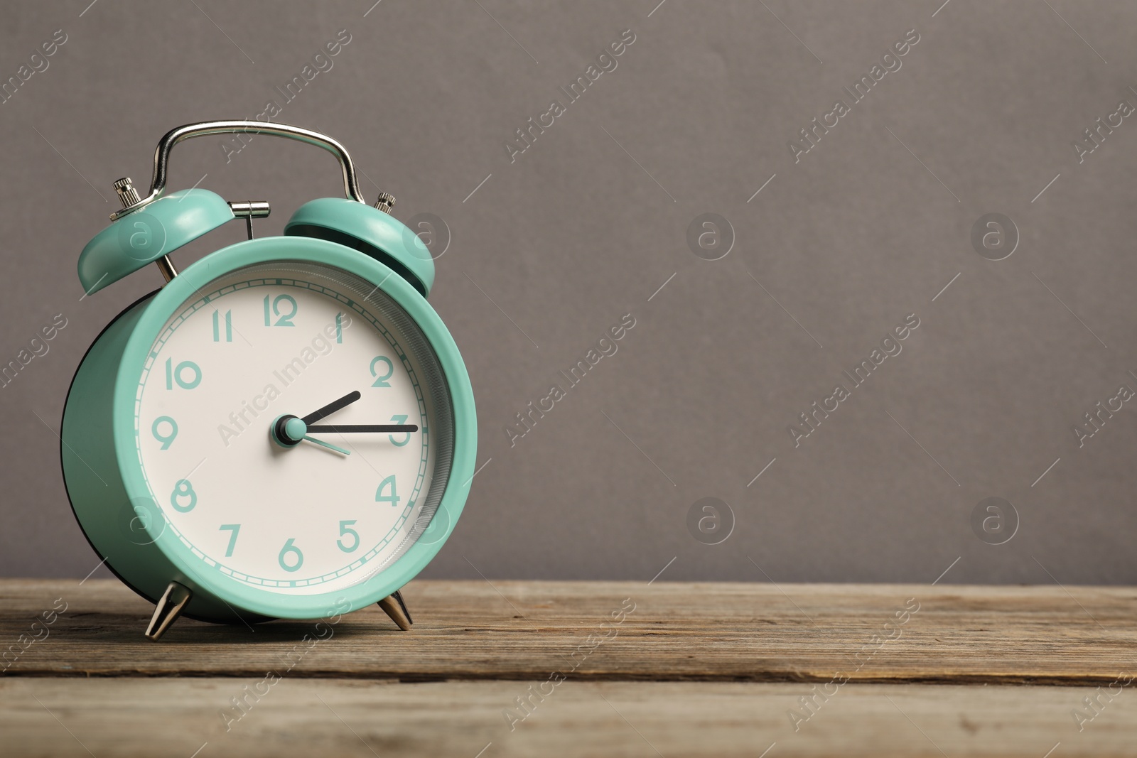 Photo of One turquoise alarm clock on wooden table against grey background, space for text