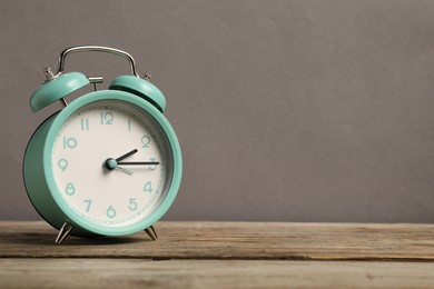 Photo of One turquoise alarm clock on wooden table against grey background, space for text