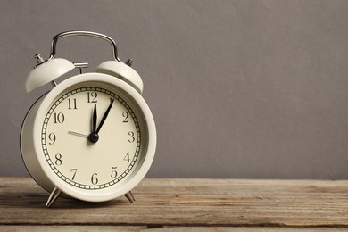 Photo of One white alarm clock on wooden table against grey background, space for text