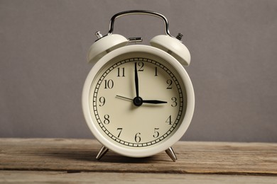 Photo of One white alarm clock on wooden table against grey background