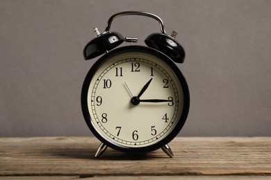 Photo of One black alarm clock on wooden table against grey background