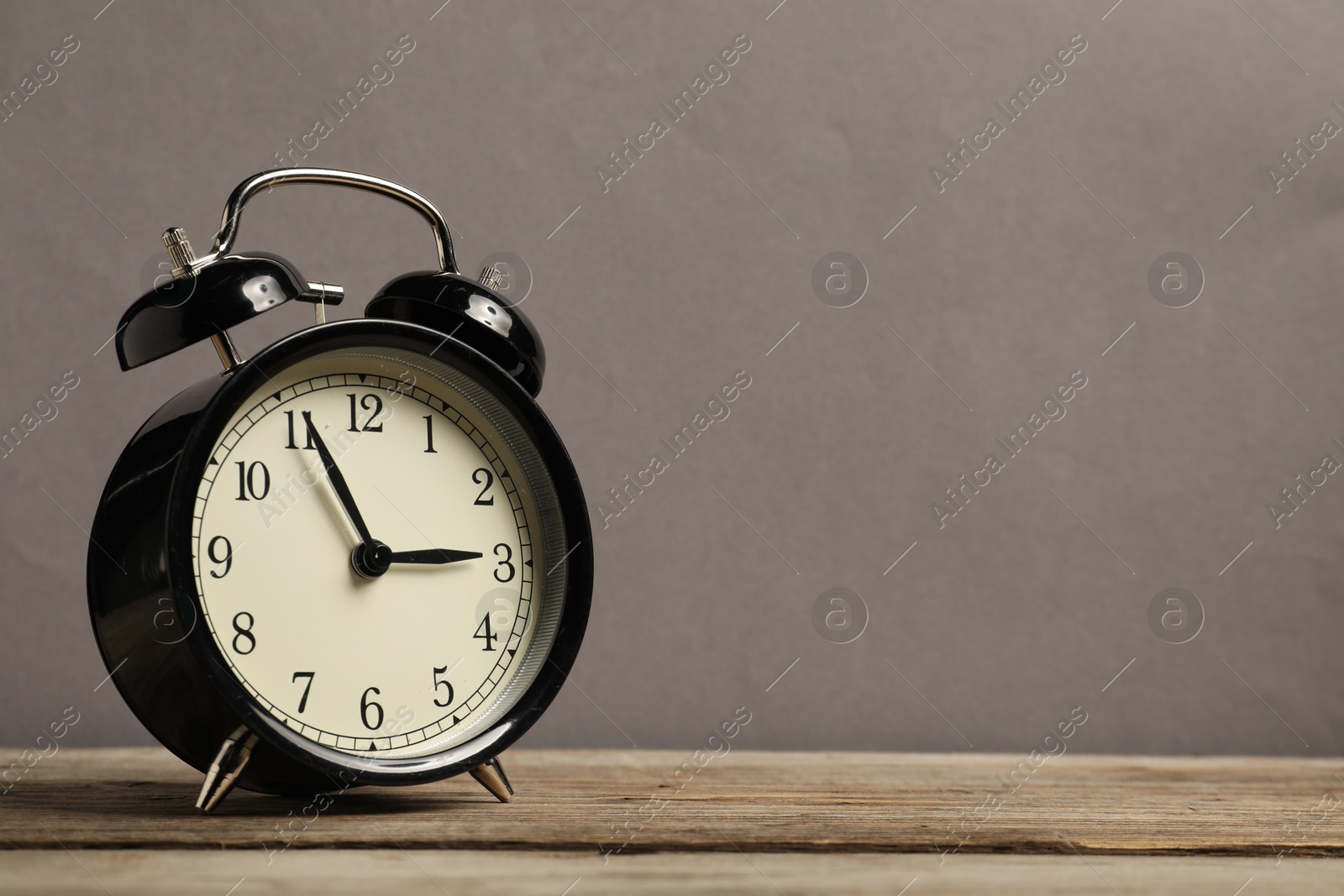 Photo of One black alarm clock on wooden table against grey background, space for text