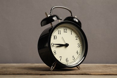 Photo of One black alarm clock on wooden table against grey background