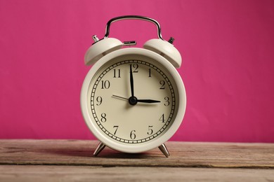 Photo of One white alarm clock on wooden table against bright pink background