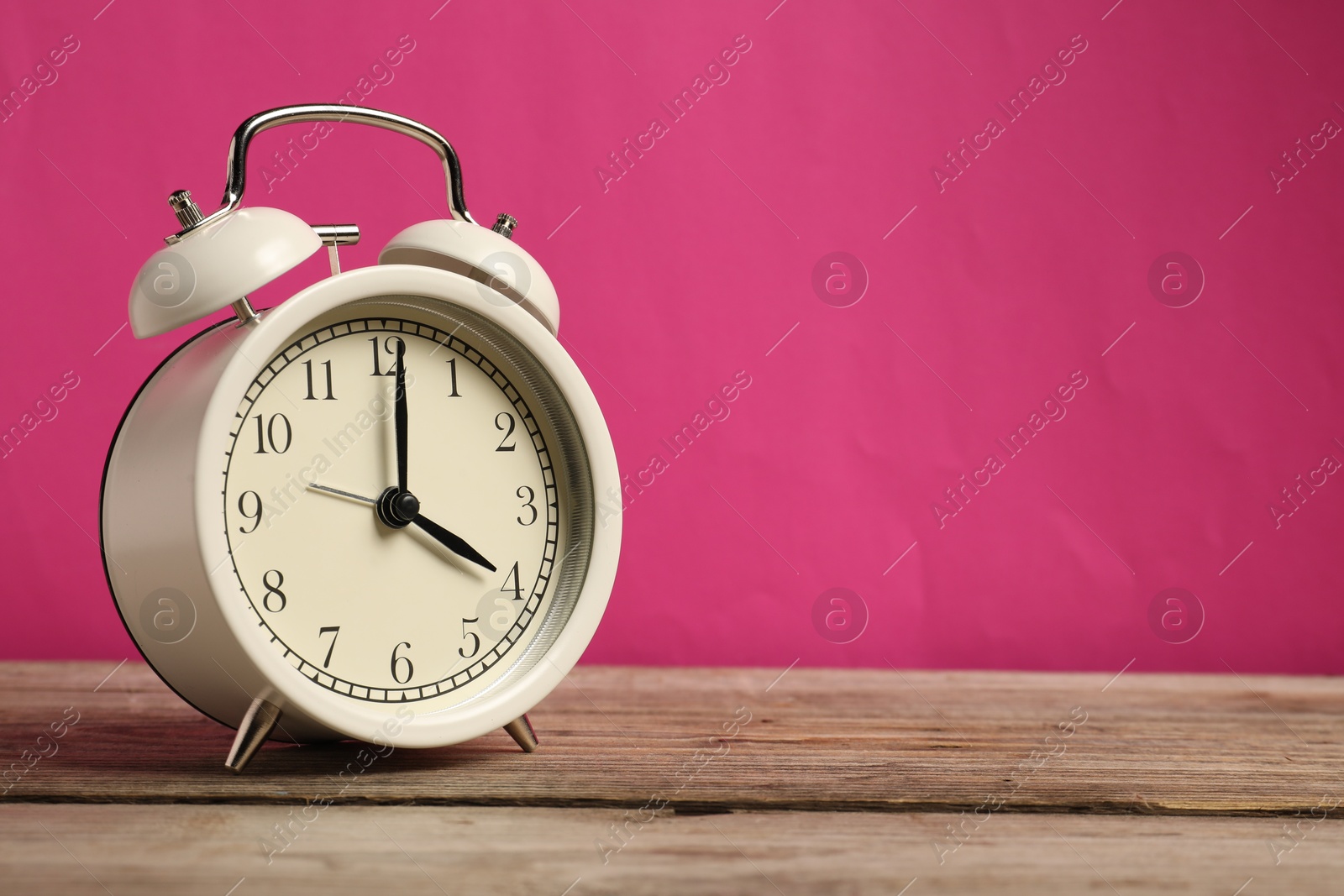 Photo of One white alarm clock on wooden table against bright pink background, space for text