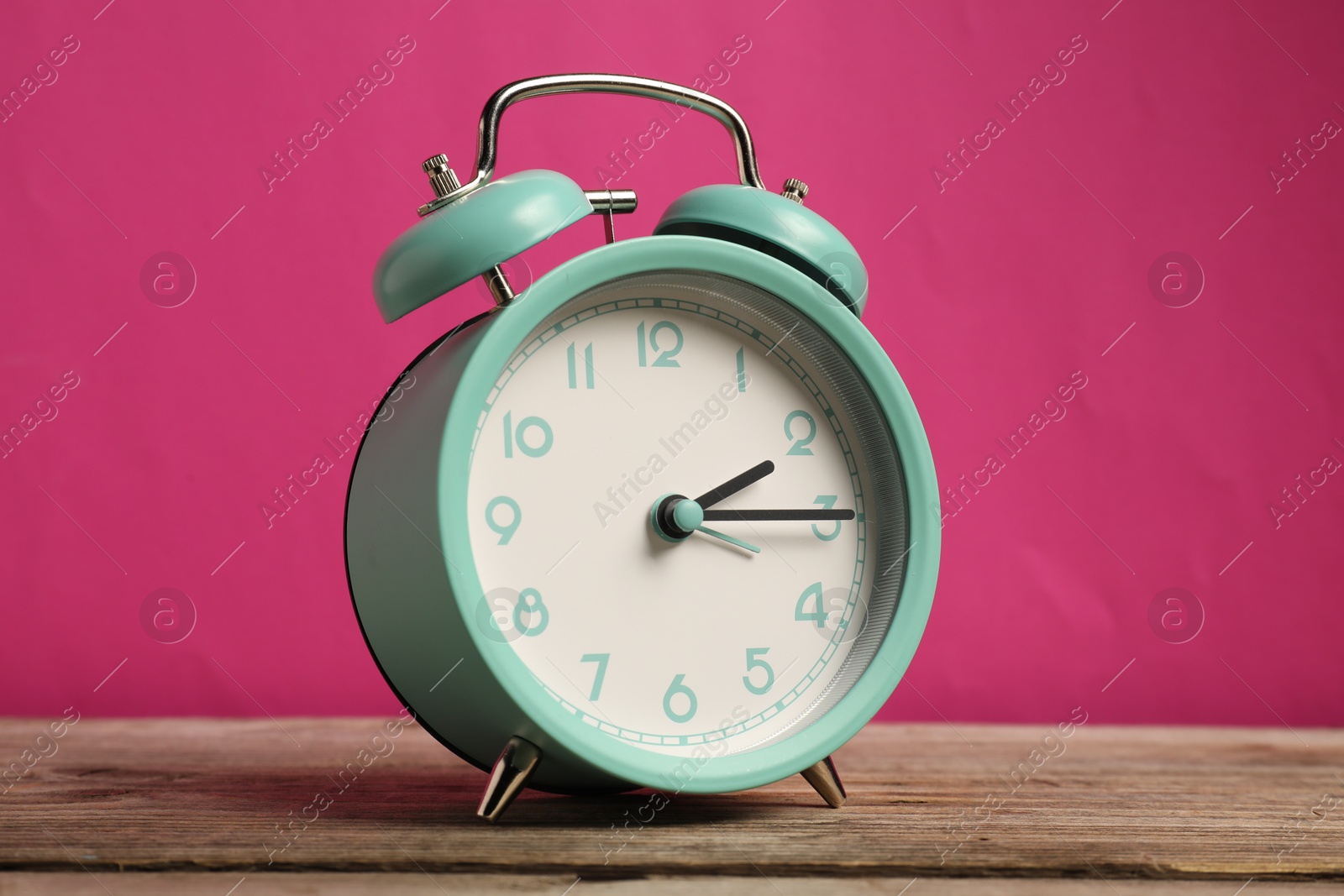 Photo of One turquoise alarm clock on wooden table against bright pink background